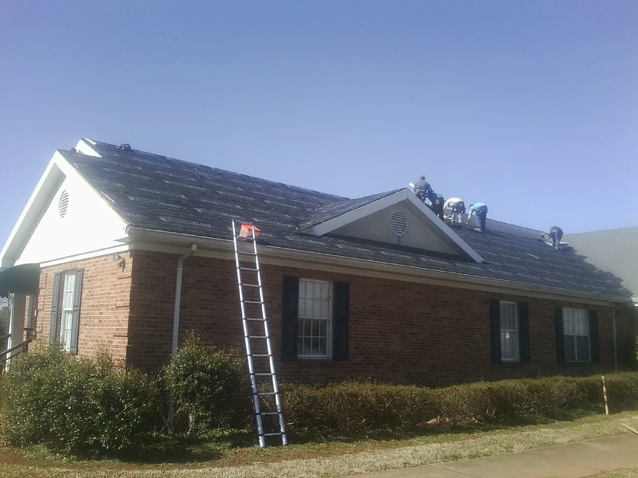 Crew tearing shingles off a brick ranch roof with a ladder set — Emergency Roof Repair work by our crew in Myrtle Beach