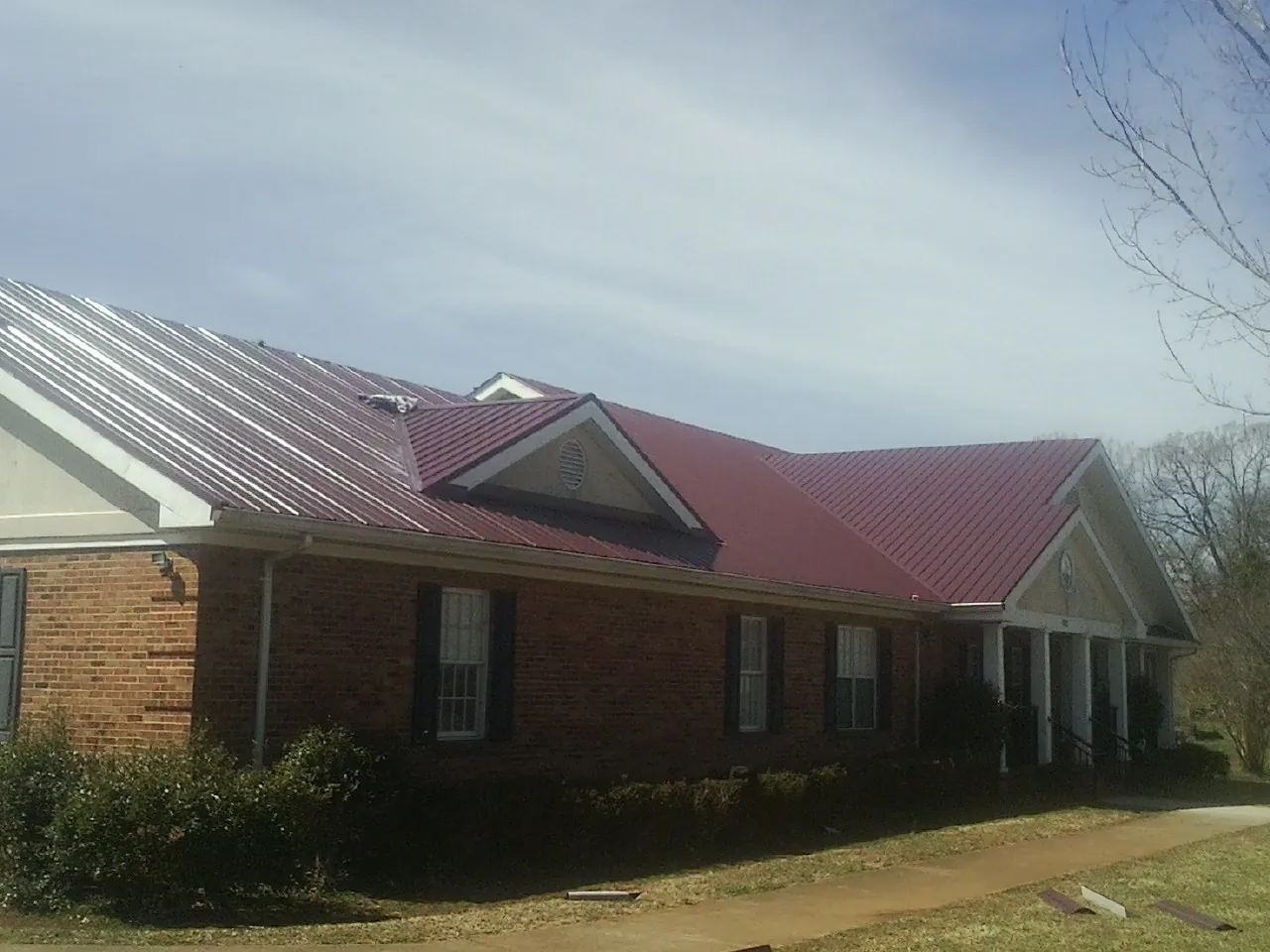 Red metal roof with gabled entries on a long brick building, from a Hail Damage Roof Repair job in Myrtle Beach