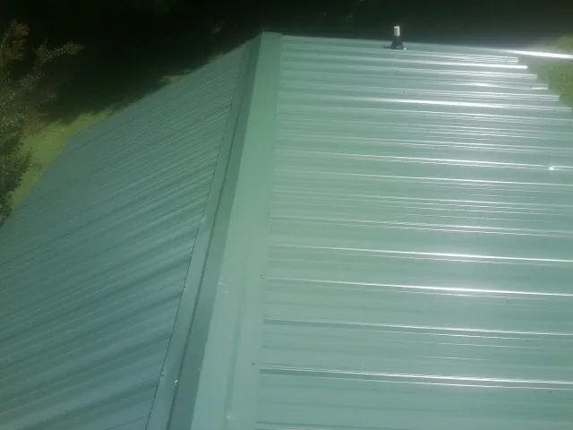 New green metal panels meeting at the ridge of a roof — Flat Roof Repair work by our crew in Myrtle Beach