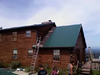 Green metal roof going on a two story log home with ladders set in Myrtle Beach