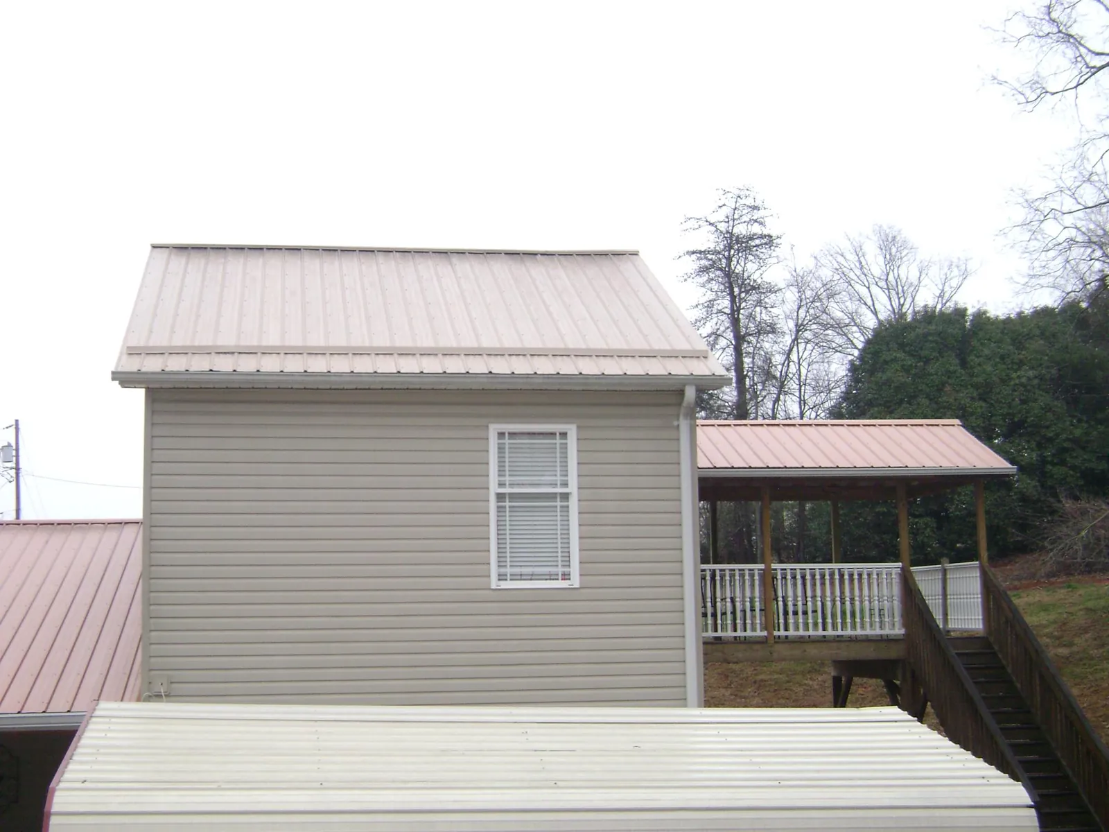 Tan metal roofs on a two story addition and attached porch, from a Roof Replacement job in Myrtle Beach